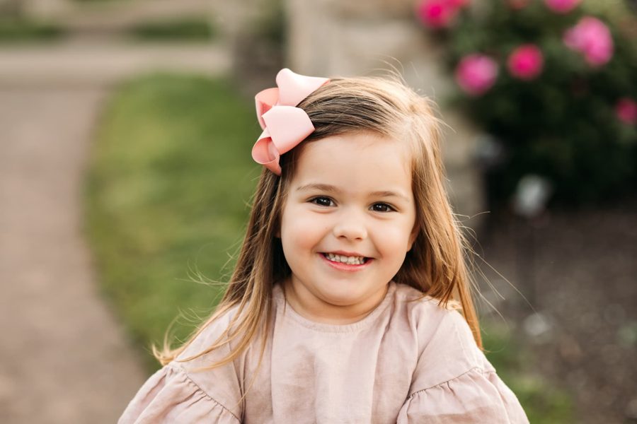 Close-up of a little girl with a pink bow smiling in the garden — family photography in the Kansas City area