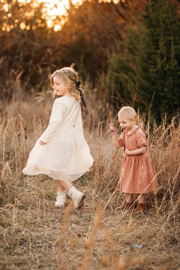 Two little sisters walking through tall autumn grasses at sunset — family photography in the Kansas City area
