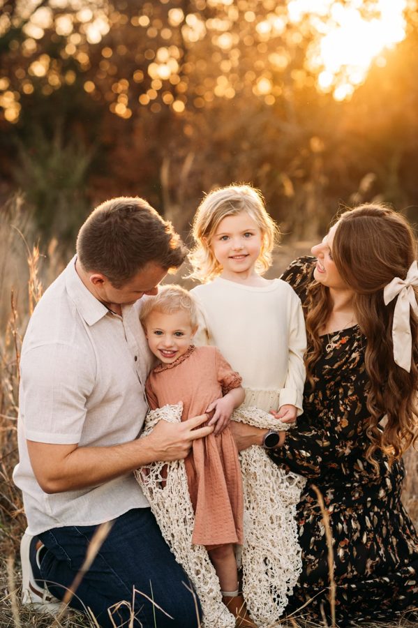 Parents kneeling with their two little girls in warm golden light — family photography in the Kansas City area