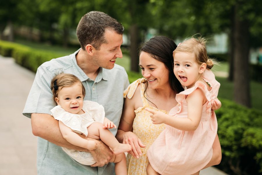 Parents laughing with their baby and toddler daughter on a summer walk — family photography in the Kansas City area