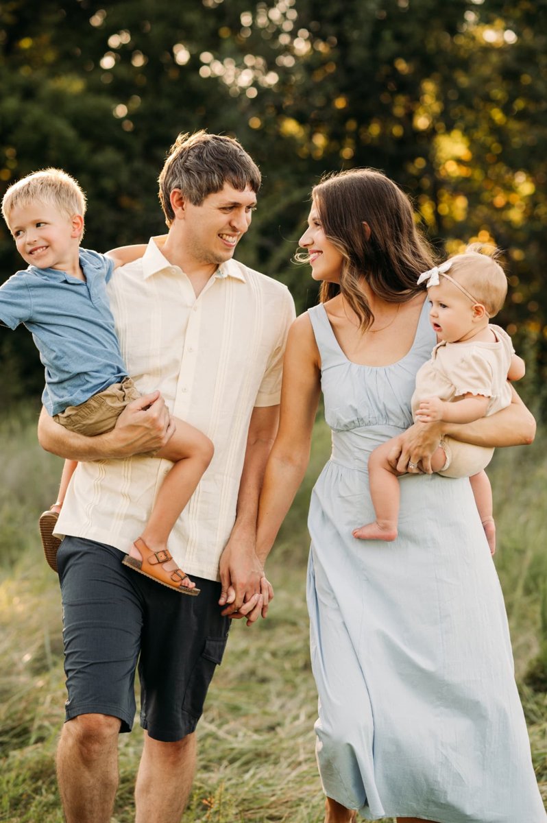 Parents walking hand in hand carrying their son and baby girl through a golden field — family photography in the Kansas City area