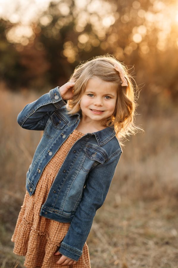 Little girl in a denim jacket smiling in a golden autumn field — family photography in the Kansas City area