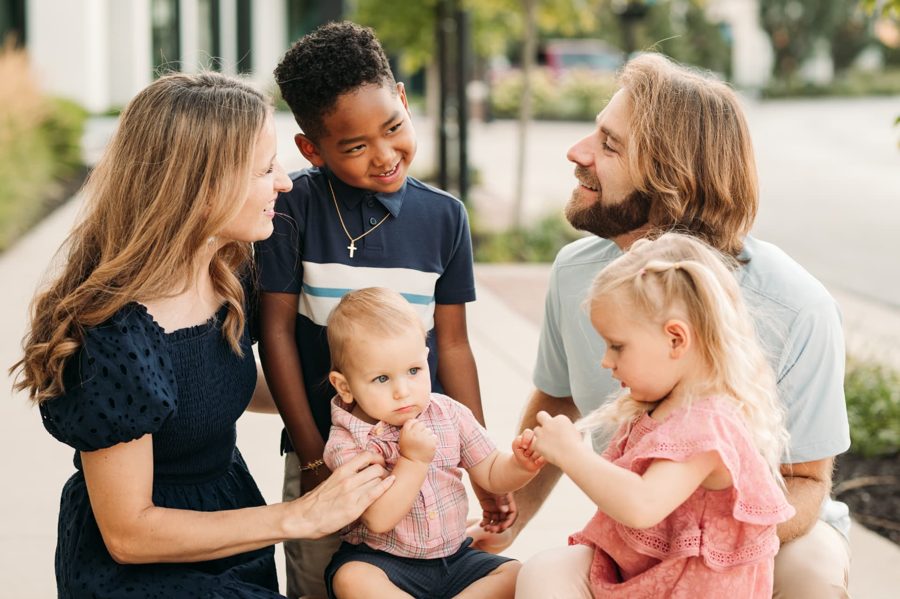 Parents kneeling and laughing with their four kids on a city sidewalk — family photography in the Kansas City area