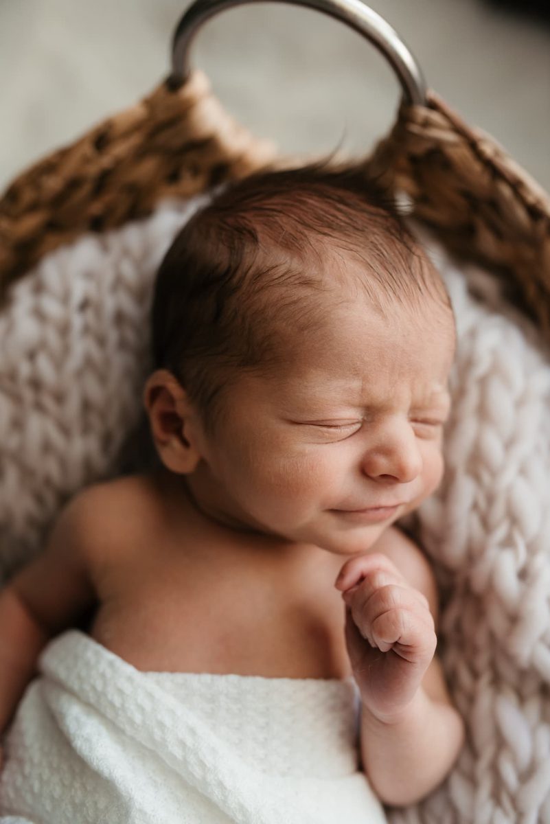 Close-up of a newborn scrunching her face while asleep in a basket — newborn photography in the Kansas City area