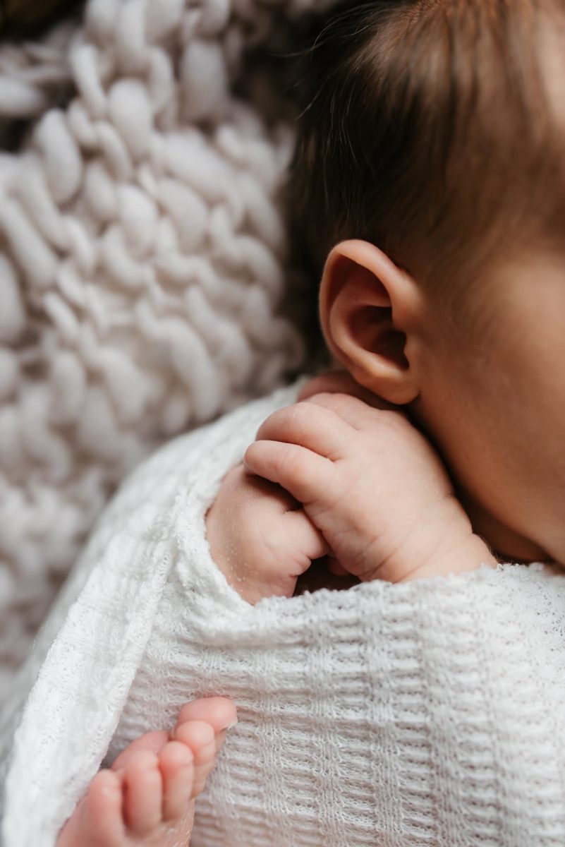 Close-up of a newborn's hands and toes peeking from a white knit wrap — newborn photography in the Kansas City area