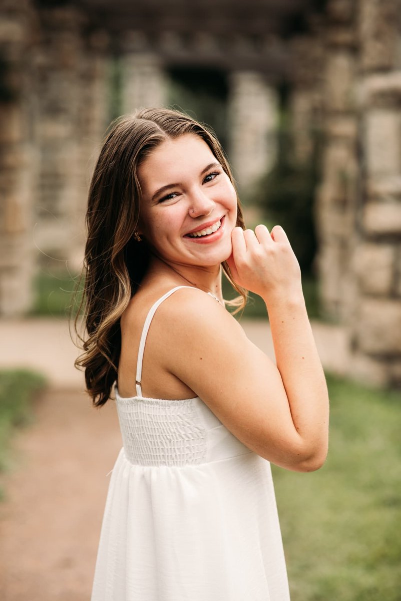 Senior girl in a white dress smiling near a stone pergola — seniors photography in the Kansas City area