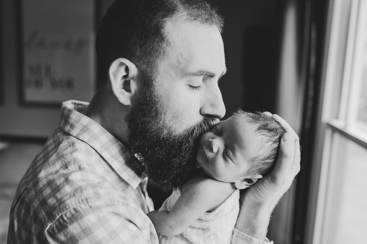 Black and white portrait of a father kissing his newborn in window light — newborn photography in the Kansas City area