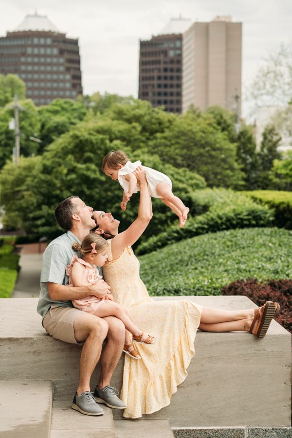 Mom lifting her baby into the air with the Kansas City skyline behind them — family photography in the Kansas City area