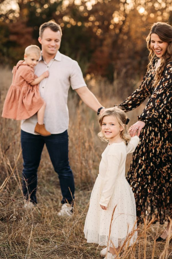 Little girl twirling with her parents in tall autumn grasses — family photography in the Kansas City area