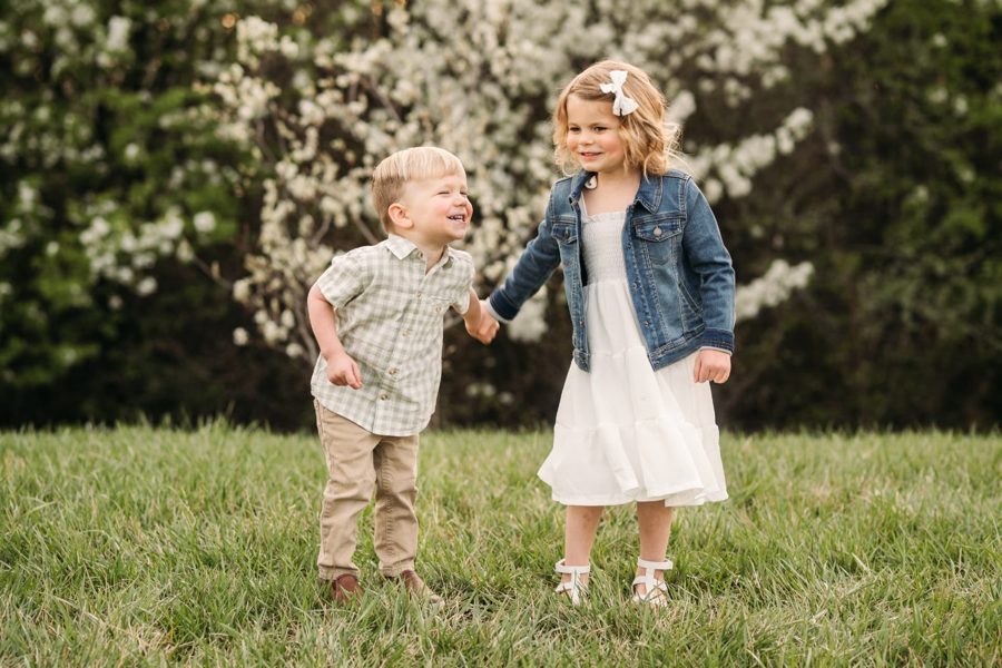 Brother and sister holding hands in a spring field of blossoms — family photography in the Kansas City area