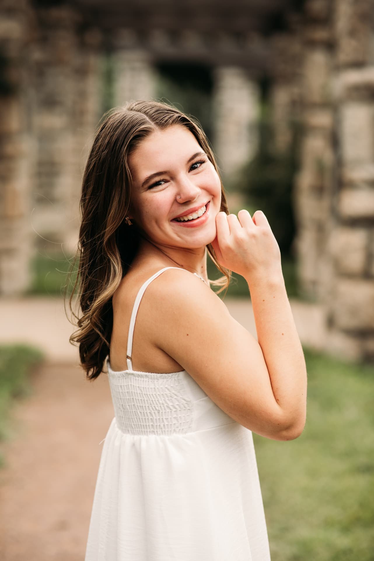 Senior girl in a white dress smiling near a stone pergola