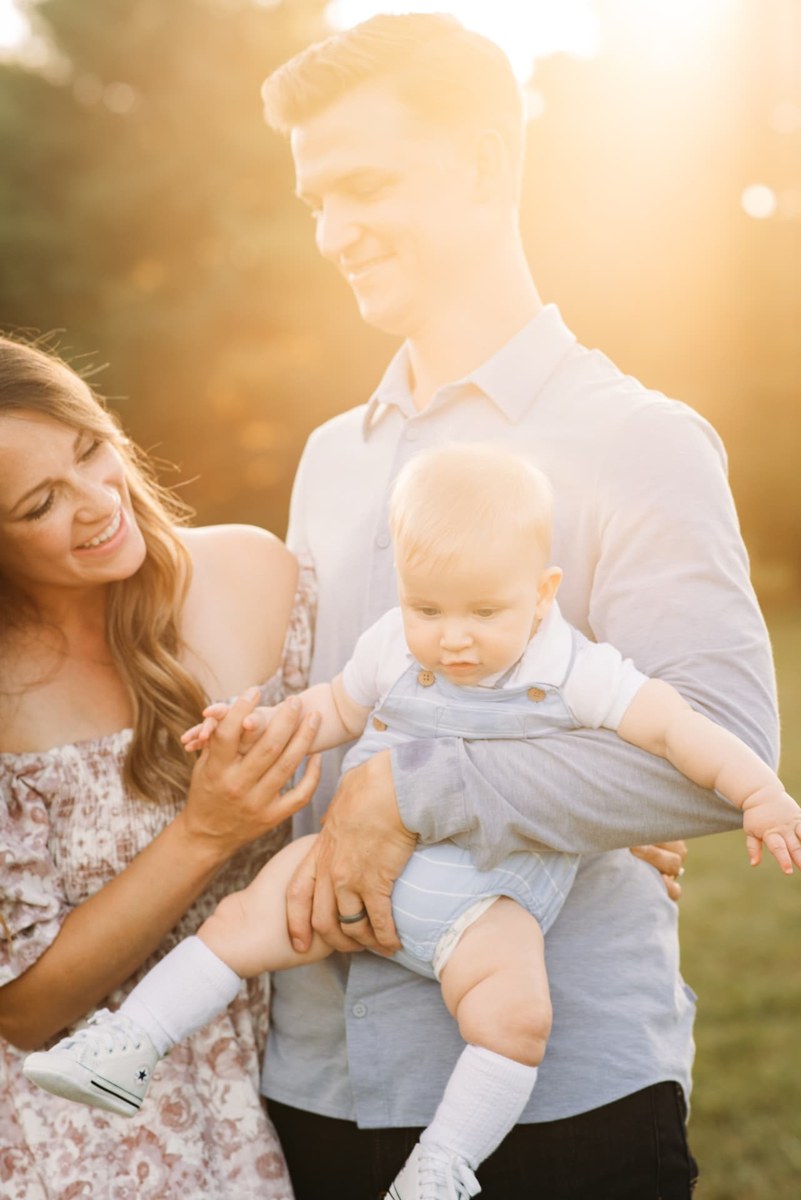 Parents holding their baby boy in warm backlit sunset light — family photography in the Kansas City area