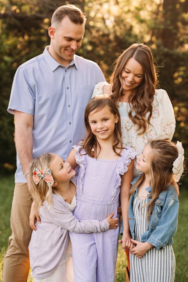 Parents and three little girls snuggled together in golden evening light — family photography in the Kansas City area