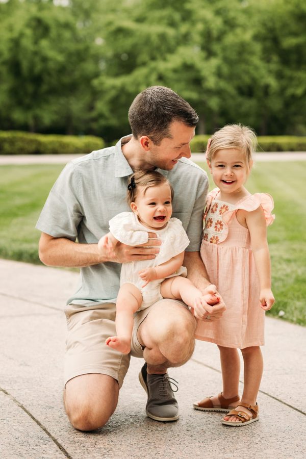 Dad kneeling with his baby and big sister on a summer afternoon — family photography in the Kansas City area