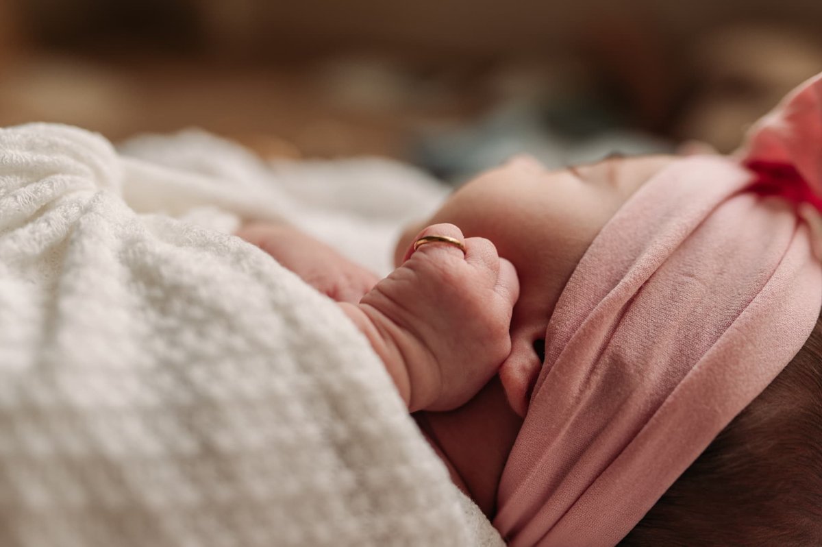 Tiny newborn fist wearing a gold ring beside her pink headband — newborn photography in the Kansas City area