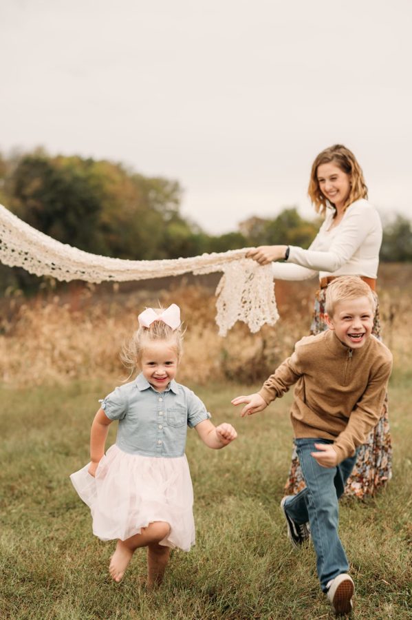 Kids running and laughing while mom holds a lace blanket in the wind — family photography in the Kansas City area