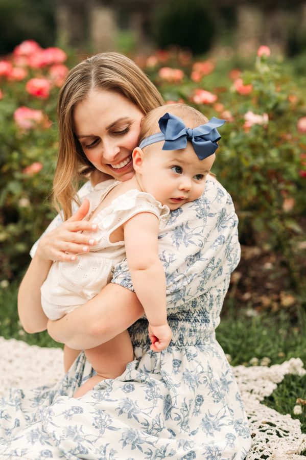 Mother in a floral dress holding her baby girl in the Kansas City rose garden — family photography in the Kansas City area
