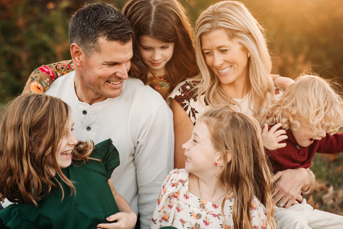 Parents and four children laughing together in warm autumn light — family photography in the Kansas City area