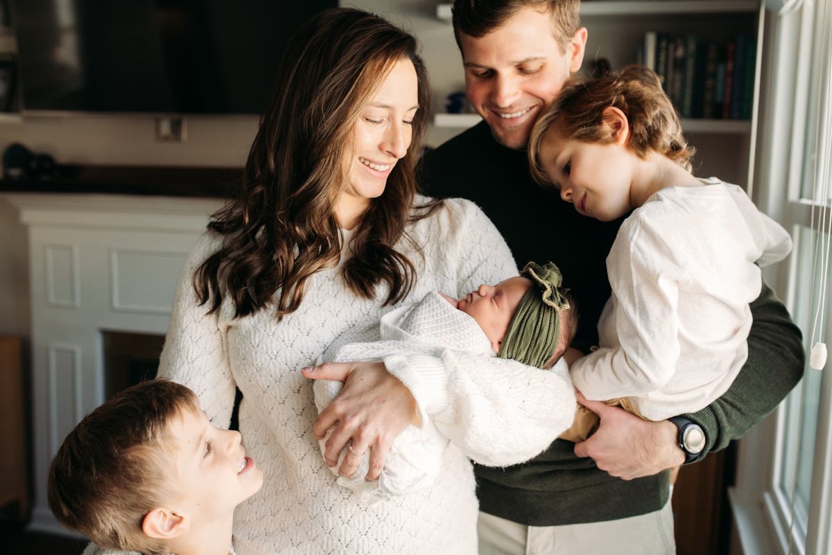 Family of five at home in window light with their newborn daughter