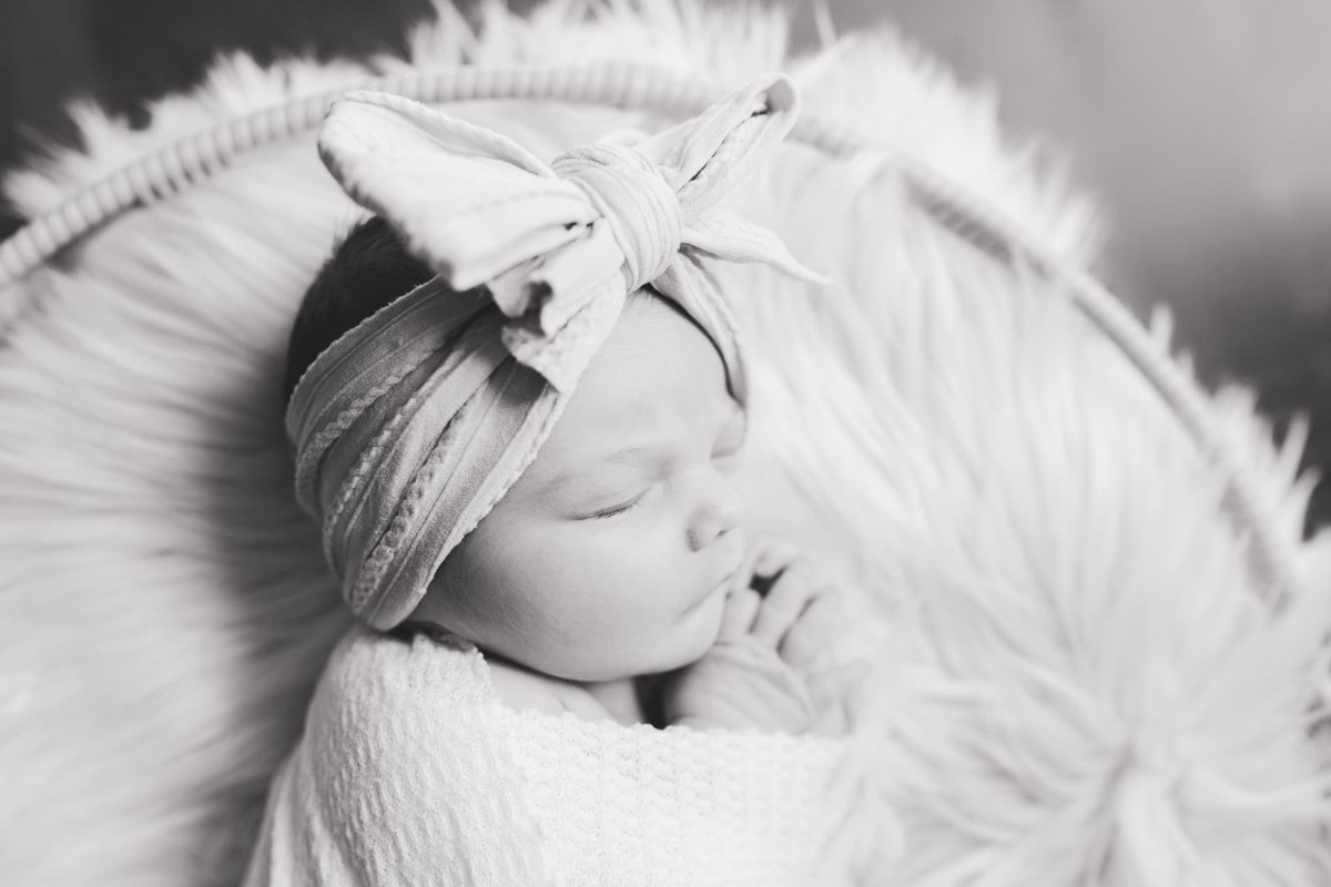 Black and white close-up of a sleeping swaddled newborn with a bow headband — newborn photography in the Kansas City area