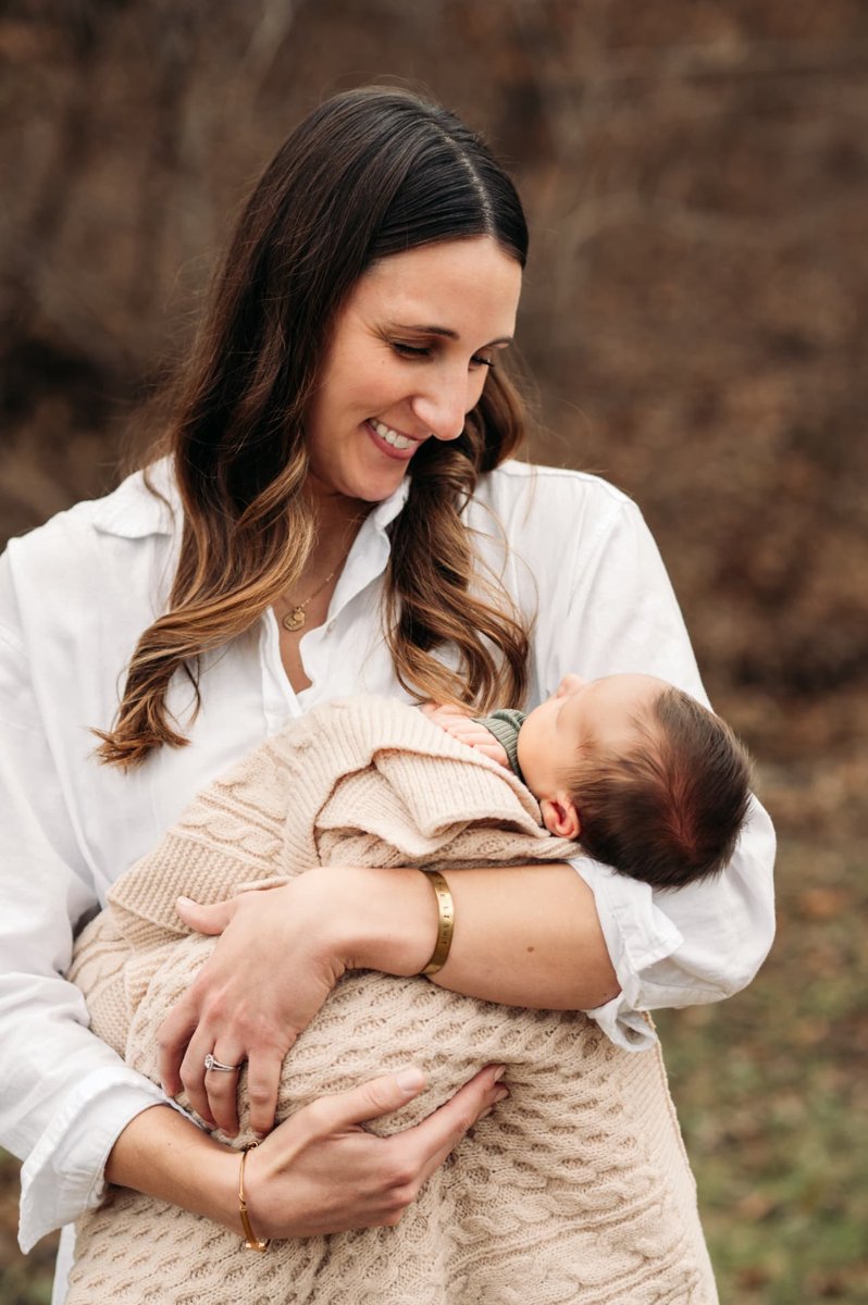 Mother cradling her newborn wrapped in a cream knit blanket outdoors — newborn photography in the Kansas City area