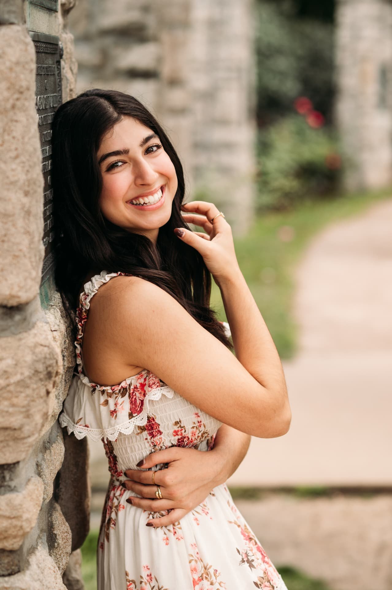 Senior girl in a floral dress laughing against a stone wall