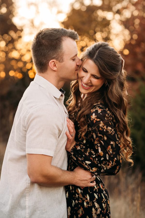 Husband kissing his wife's cheek as she laughs at golden hour — family photography in the Kansas City area