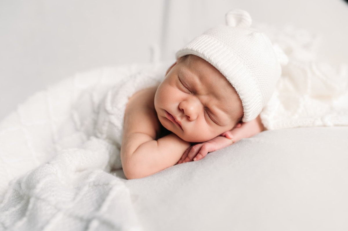 Newborn in a white knit bear hat resting his head on his hands — newborn photography in the Kansas City area