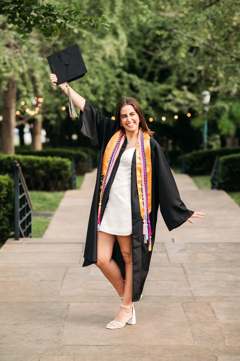 Senior girl in cap and gown celebrating on a tree-lined walkway