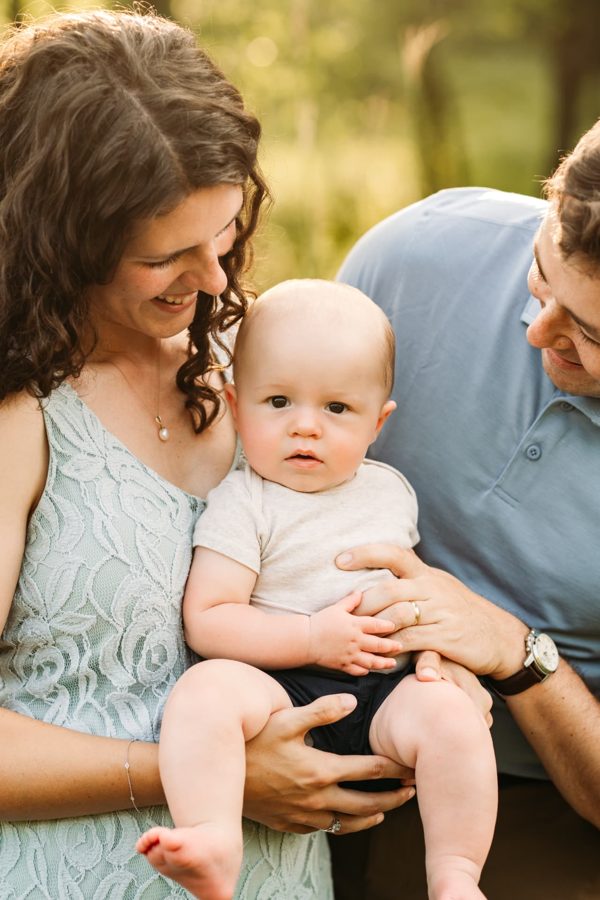 Parents smiling down at their baby boy in soft evening light — family photography in the Kansas City area