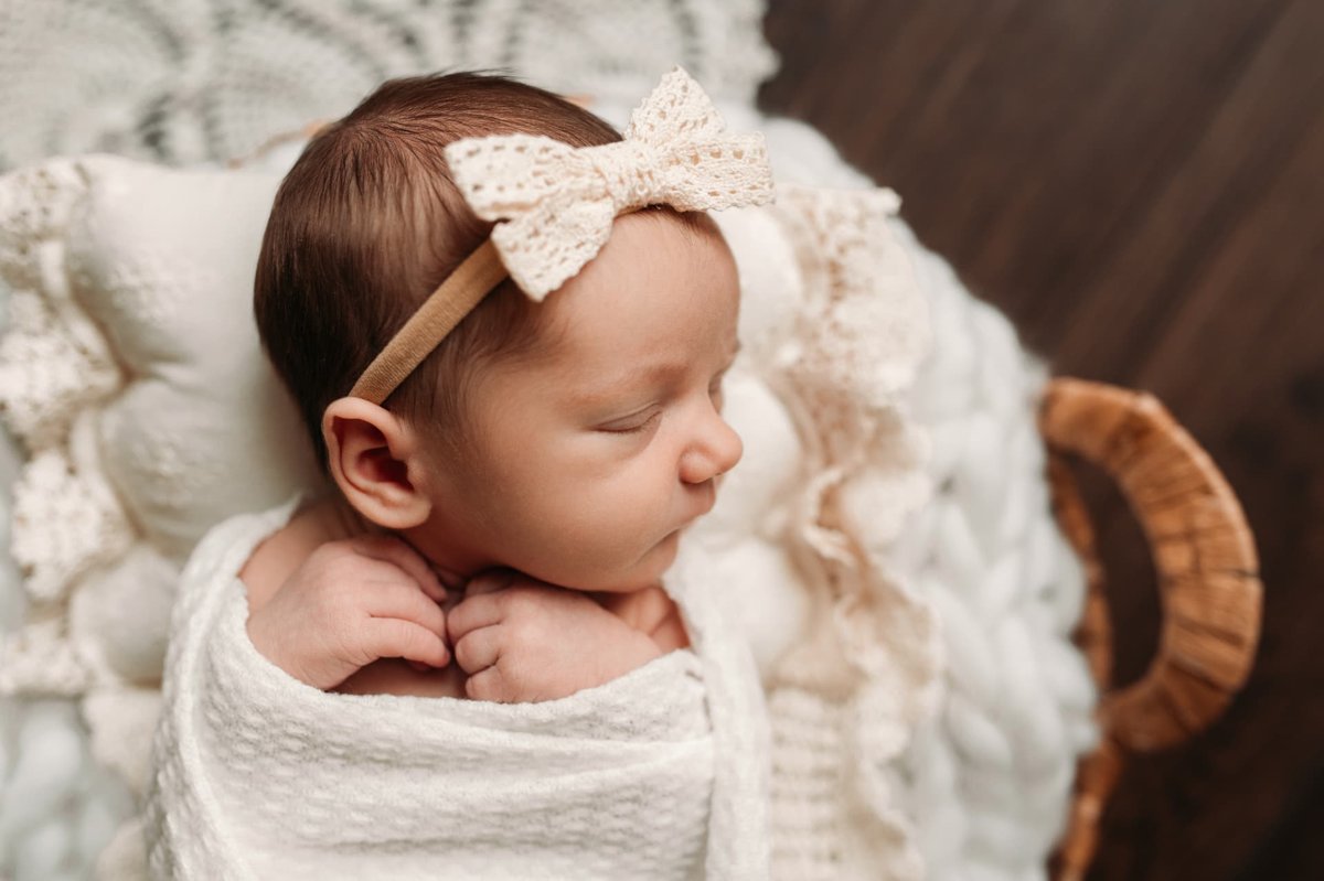 Close-up of a sleeping newborn girl in a cream lace bow — newborn photography in the Kansas City area
