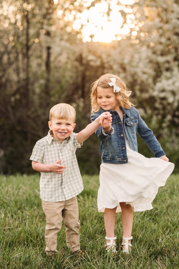 Siblings twirling and laughing at golden hour beneath blossoming trees — family photography in the Kansas City area