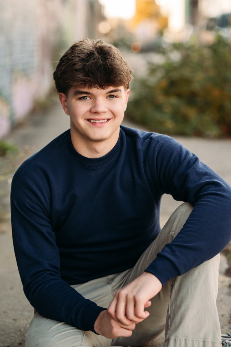 Senior guy in a navy shirt sitting in a mural alley at sunset — seniors photography in the Kansas City area