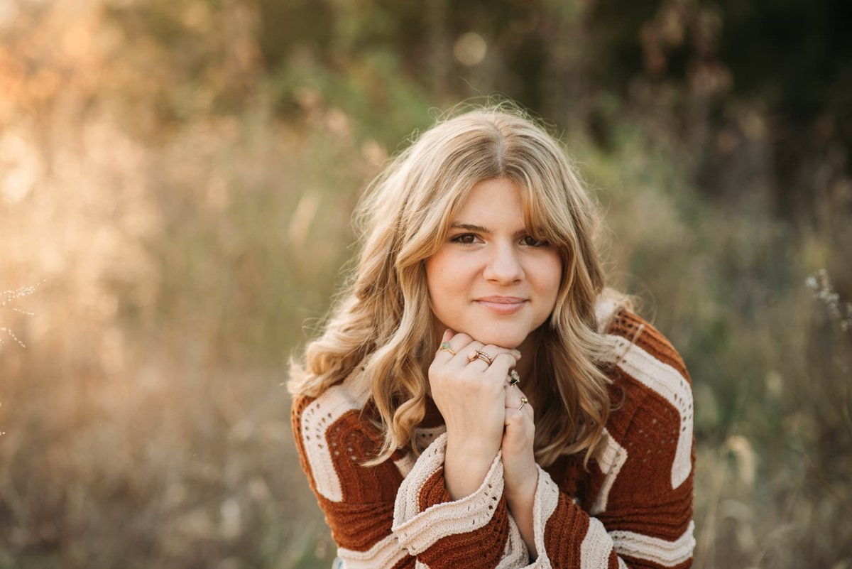 Senior girl in a rust knit sweater at golden hour in a Kansas field