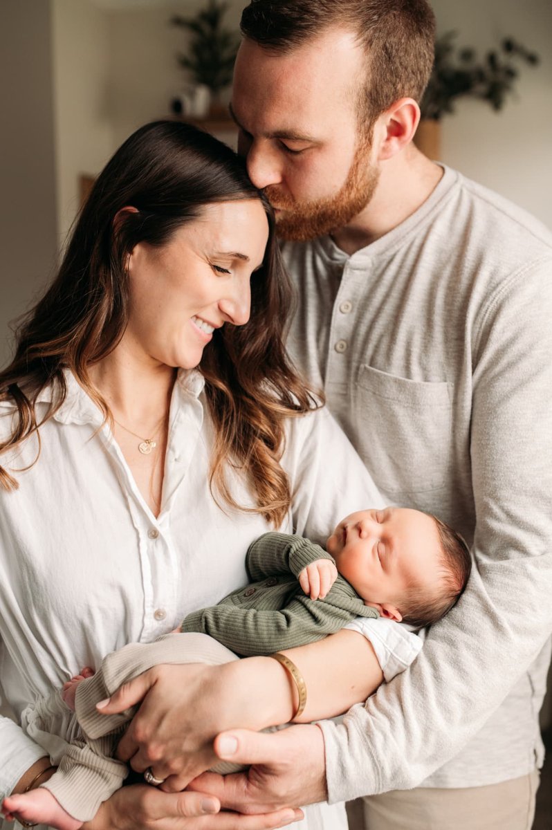 Father kissing mother's forehead while she cradles their newborn son — newborn photography in the Kansas City area