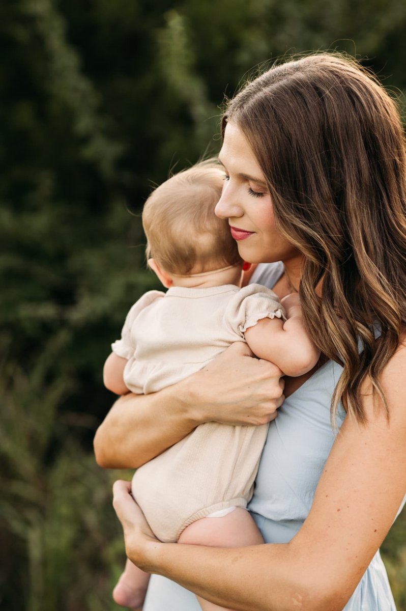 Mom snuggling her baby girl close with eyes closed in soft evening light — family photography in the Kansas City area