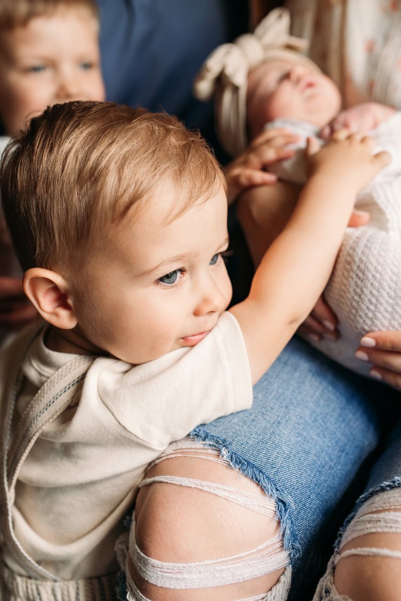 Toddler brother touching his newborn sister during an in-home session — newborn photography in the Kansas City area