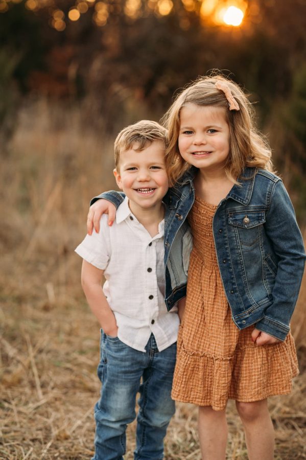 Brother and sister hugging in an autumn field at sunset — family photography in the Kansas City area