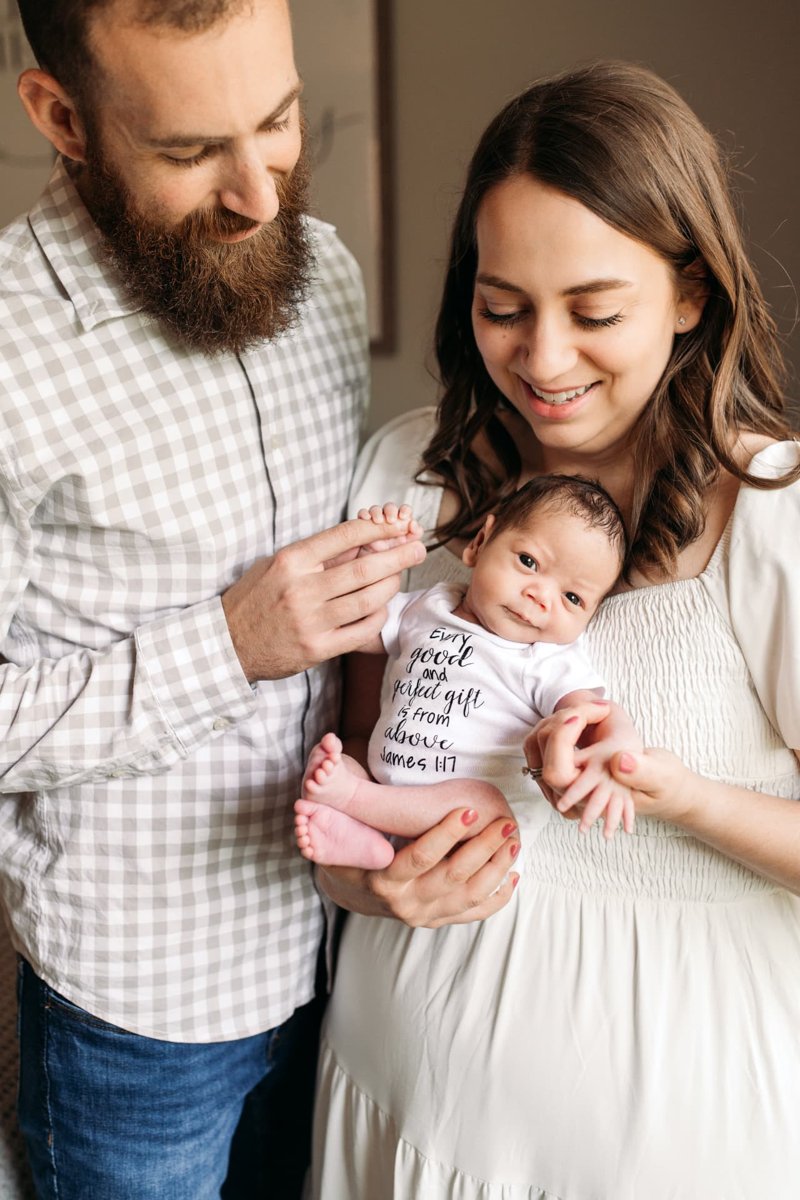 Parents smiling down at their newborn in a bright in-home session