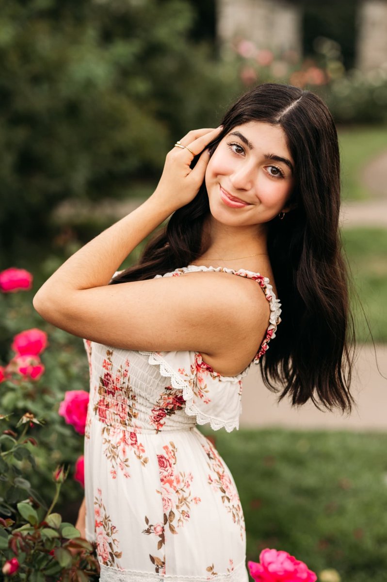 Senior girl in a floral dress beside blooming pink roses — seniors photography in the Kansas City area