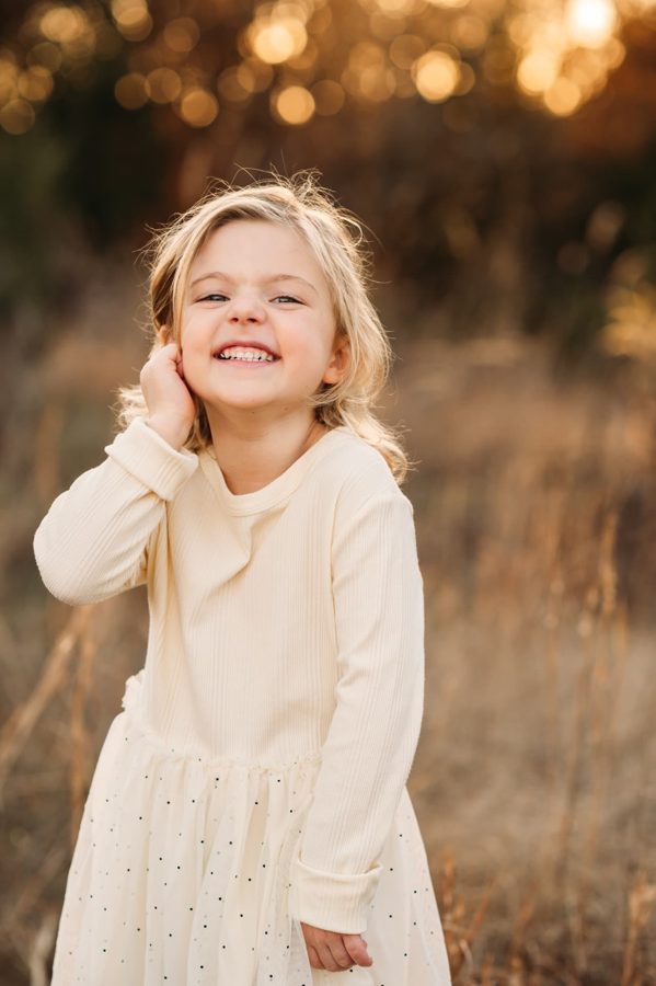 Little girl in a cream dress giggling in golden autumn light — family photography in the Kansas City area