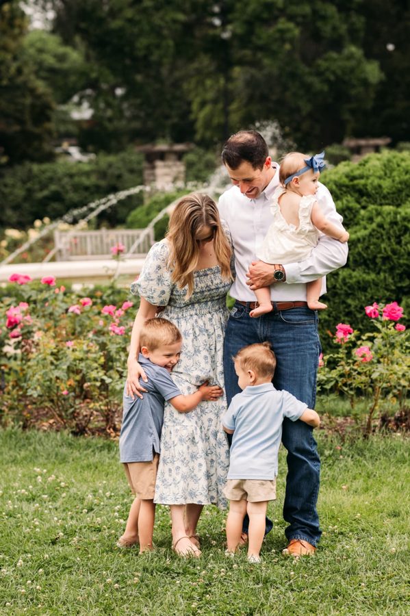 Family of five hugging together beside the fountain at the rose garden — family photography in the Kansas City area