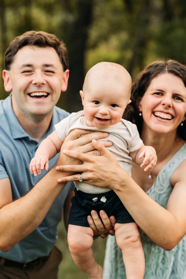 Parents holding their giggling baby boy up between them — family photography in the Kansas City area