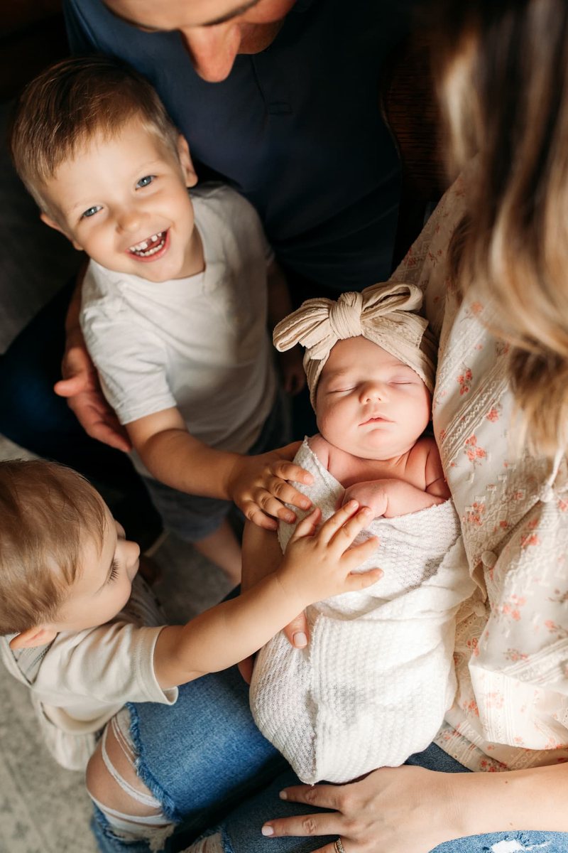 Big brothers reaching for their newborn sister in her mother's arms — newborn photography in the Kansas City area