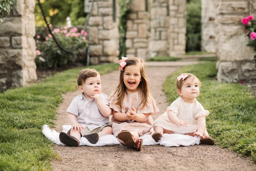 Three siblings sitting together on a blanket in the rose garden — family photography in the Kansas City area