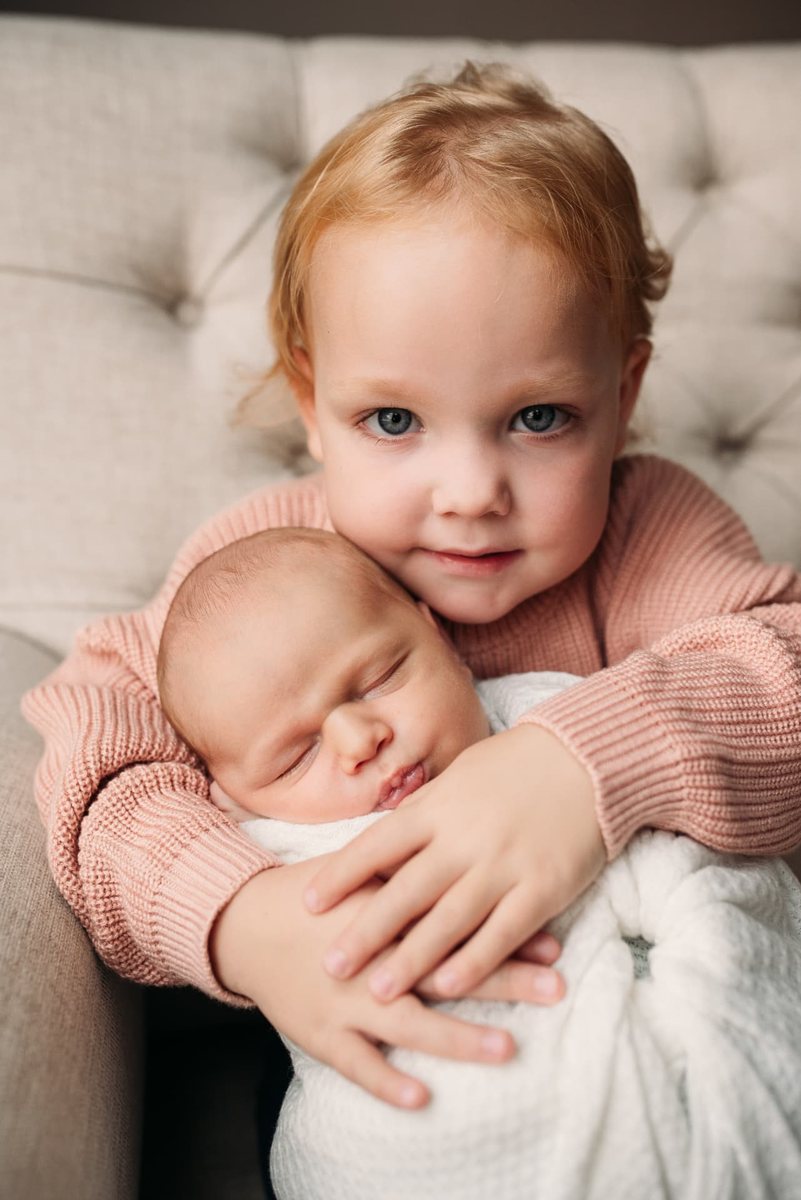 Toddler sister cuddling her sleeping newborn brother