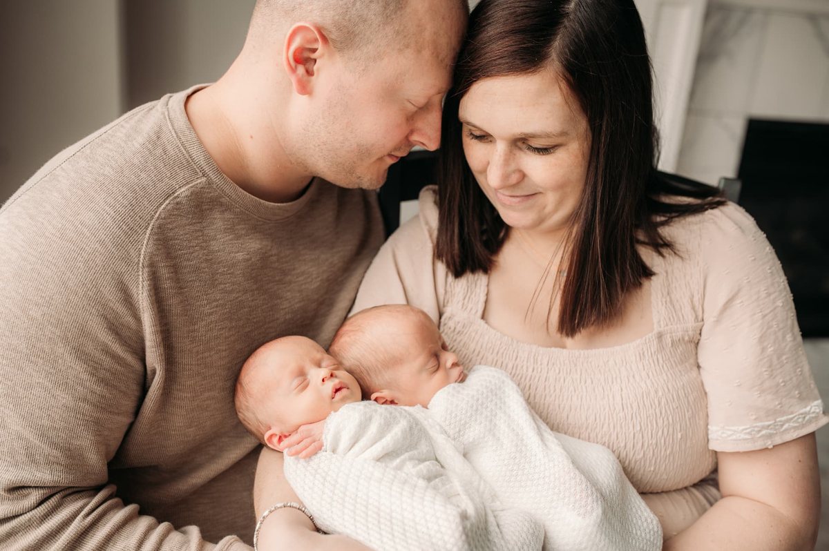 Mother and father cuddling their swaddled newborn twins