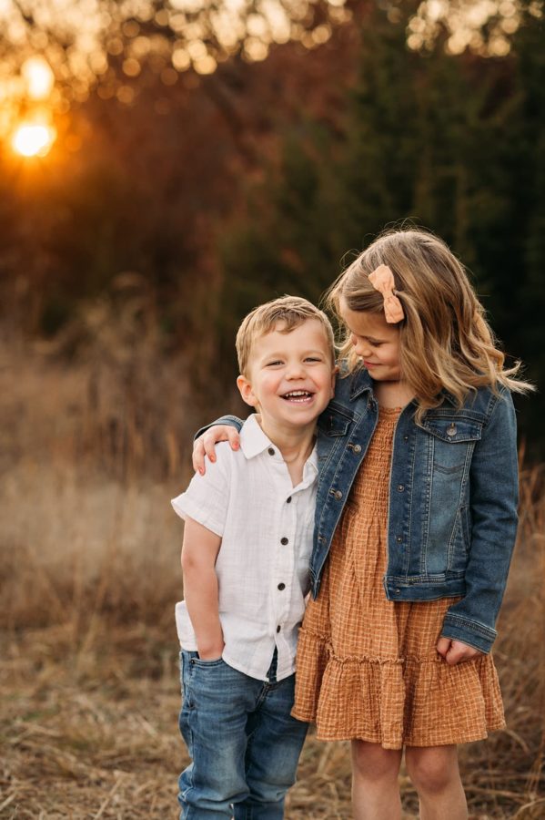 Brother and sister laughing together in a golden sunset field — family photography in the Kansas City area