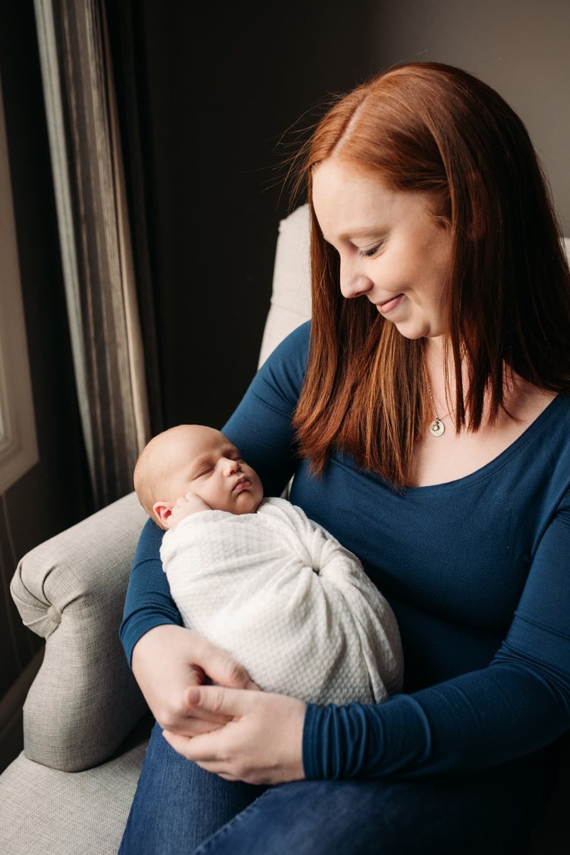 Mother holding her swaddled newborn in soft window light — newborn photography in the Kansas City area