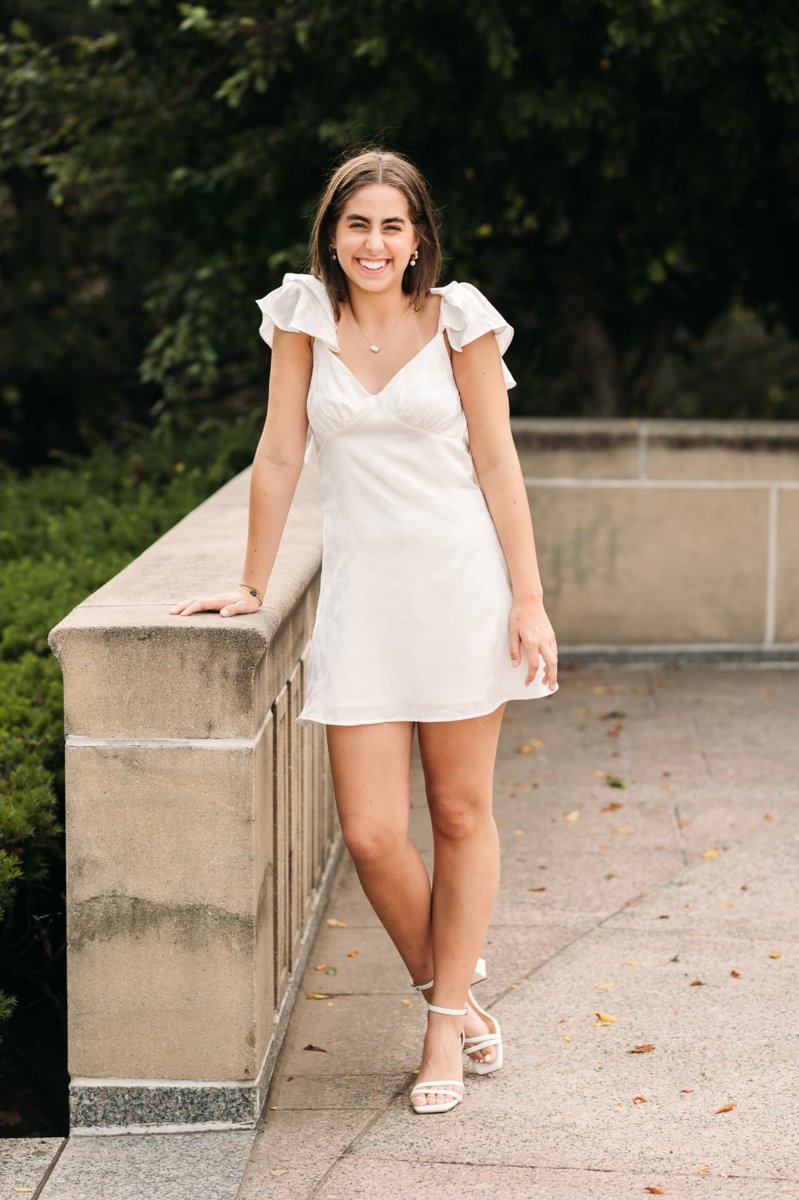 Senior girl in a white dress laughing beside a stone ledge